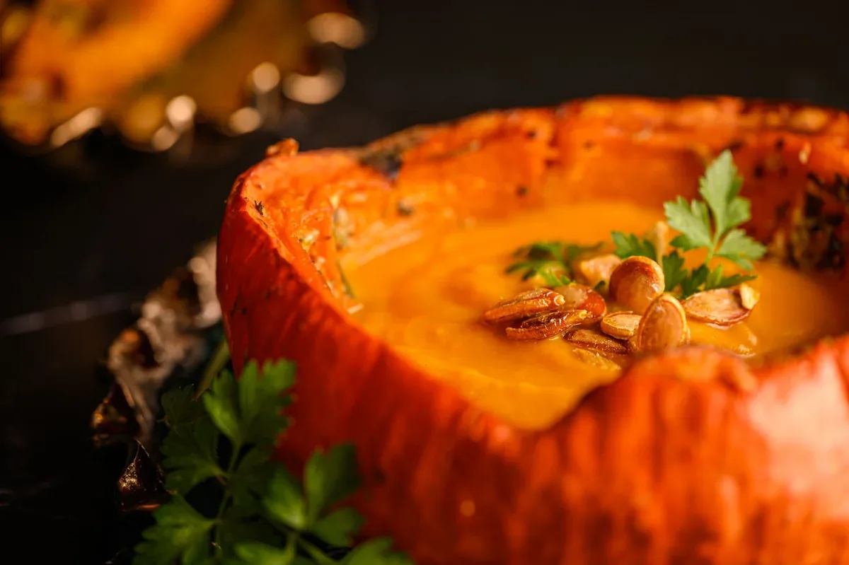 Soupe de potiron crémeuse servie dans une courge évidée, avec des graines et du persil