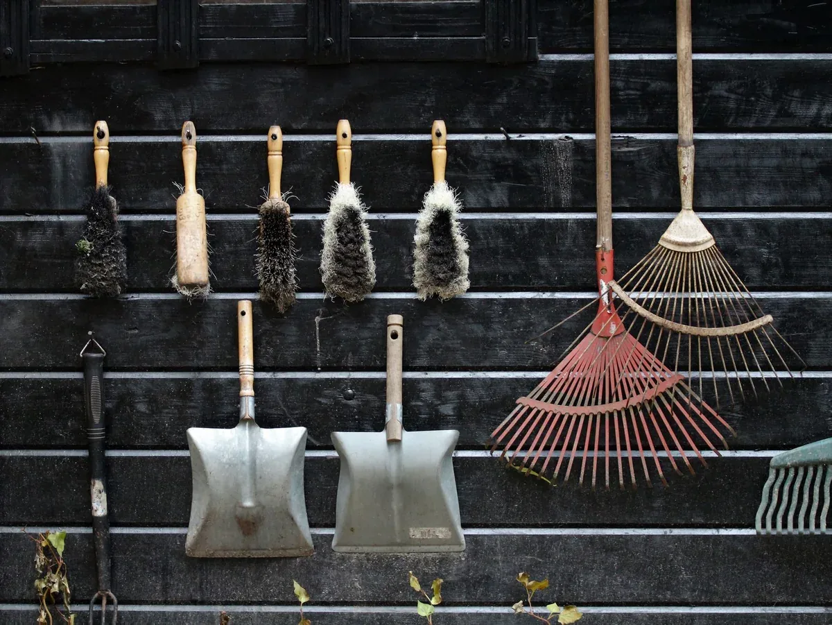 Outils de jardin nettoyés et rangés au mur : râteau, pelles, balais